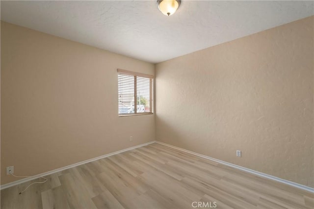 unfurnished room featuring light wood-style floors, baseboards, a textured wall, and a textured ceiling