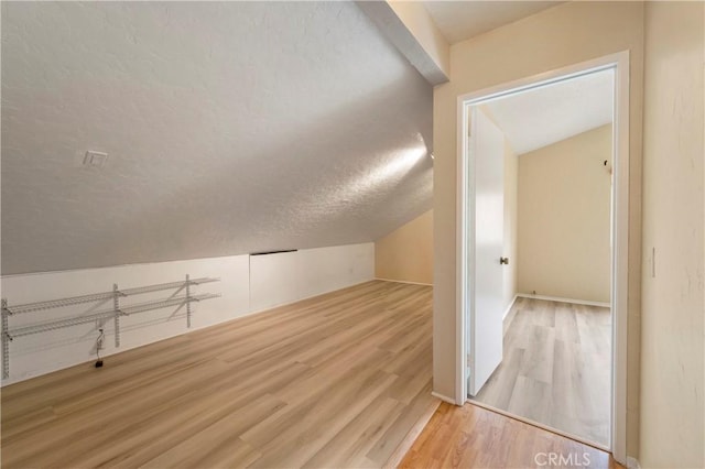 additional living space featuring lofted ceiling, a textured ceiling, and wood finished floors