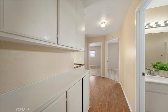 hall with light wood-style flooring, baseboards, and a sink