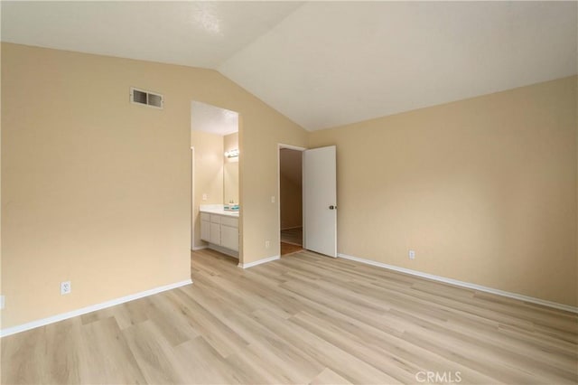 unfurnished bedroom featuring visible vents, ensuite bathroom, light wood finished floors, baseboards, and vaulted ceiling