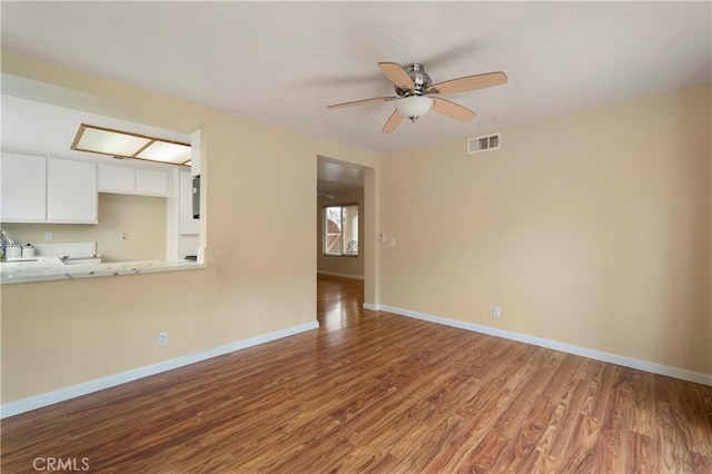 unfurnished living room with visible vents, baseboards, wood finished floors, a ceiling fan, and a sink