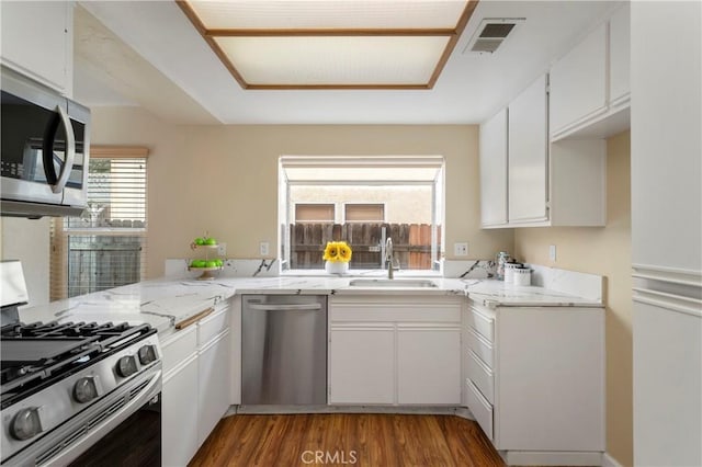 kitchen featuring visible vents, a sink, light stone counters, stainless steel appliances, and white cabinets