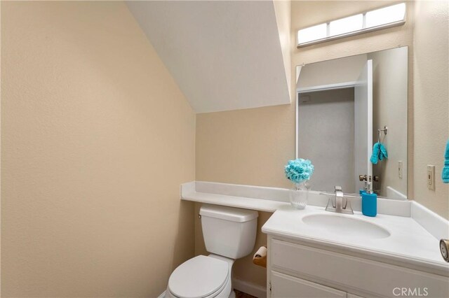 bathroom with toilet, vanity, and vaulted ceiling