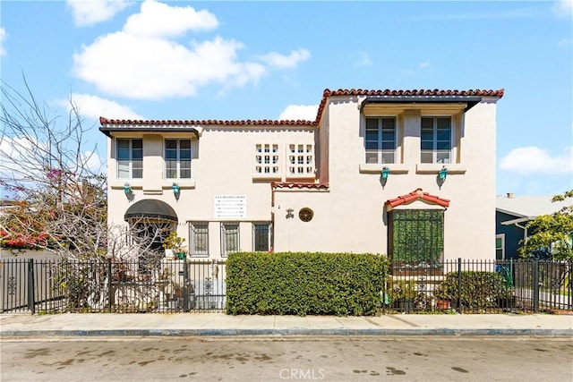 mediterranean / spanish-style house featuring stucco siding, a tile roof, and fence