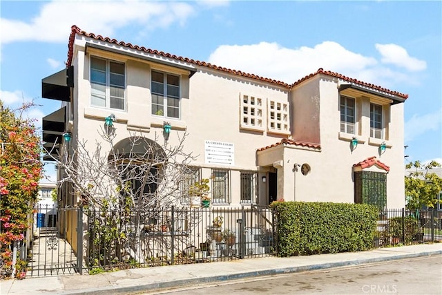 mediterranean / spanish house featuring a tile roof, fence, and stucco siding