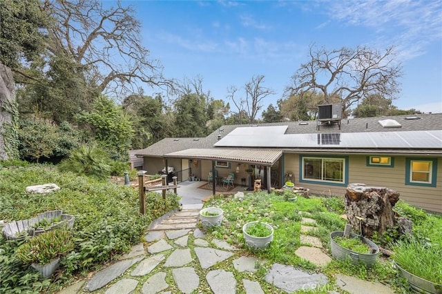 rear view of property featuring solar panels, a vegetable garden, cooling unit, and a patio area