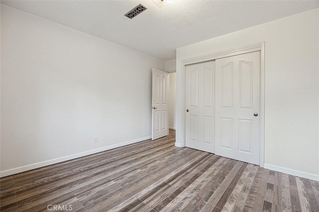 unfurnished bedroom featuring visible vents, baseboards, wood finished floors, a closet, and a textured ceiling