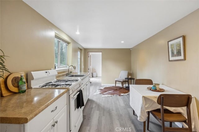 kitchen with light wood finished floors, baseboards, white gas range oven, white cabinetry, and a sink