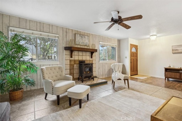 living area featuring plenty of natural light, a ceiling fan, wood walls, and a wood stove