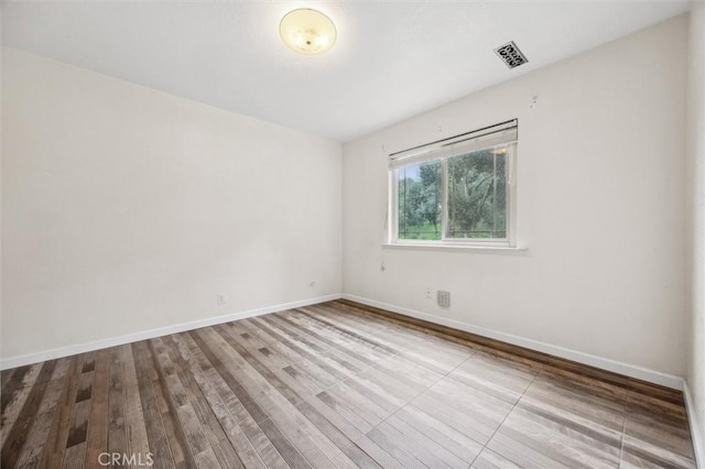 empty room featuring visible vents, baseboards, and wood finished floors