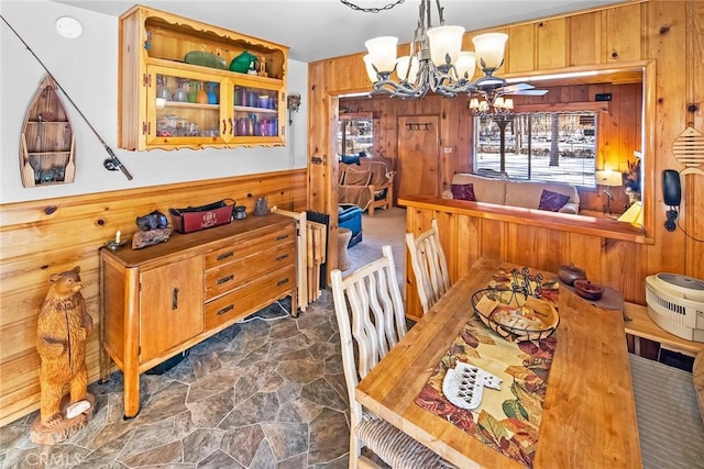 dining area featuring a notable chandelier, wood walls, and stone finish flooring