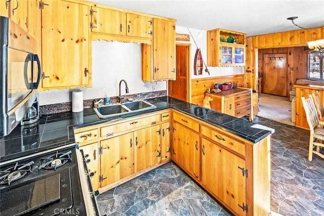 kitchen featuring a sink, stainless steel microwave, wooden walls, a peninsula, and stone flooring