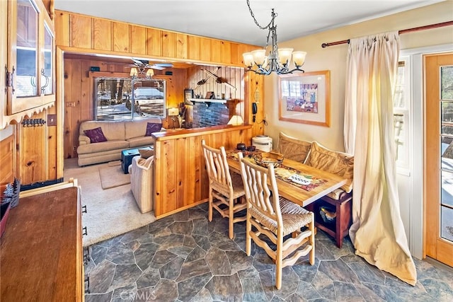 dining space featuring a notable chandelier, wood walls, stone finish flooring, and carpet