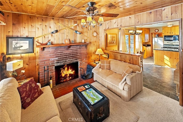 living room featuring ceiling fan with notable chandelier, wooden ceiling, wooden walls, and a fireplace