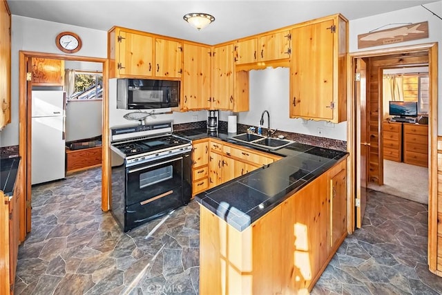 kitchen with a peninsula, black appliances, stone finish flooring, and a sink