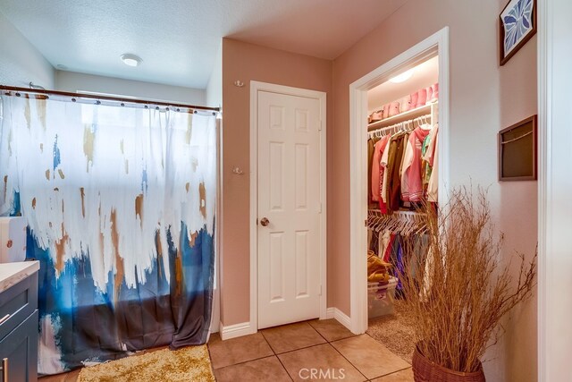 bathroom with tile patterned floors, a walk in closet, a shower with shower curtain, baseboards, and vanity