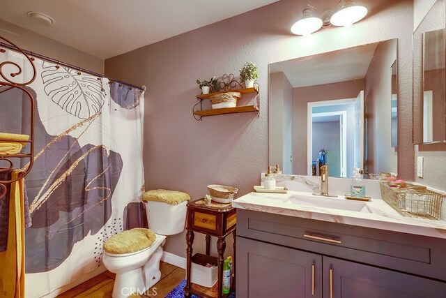 full bath featuring toilet, curtained shower, baseboards, vanity, and a textured wall