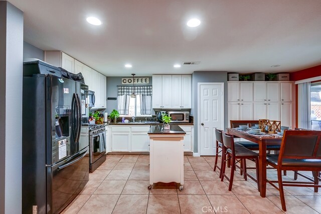 kitchen with visible vents, black fridge, stainless steel microwave, dark countertops, and gas range