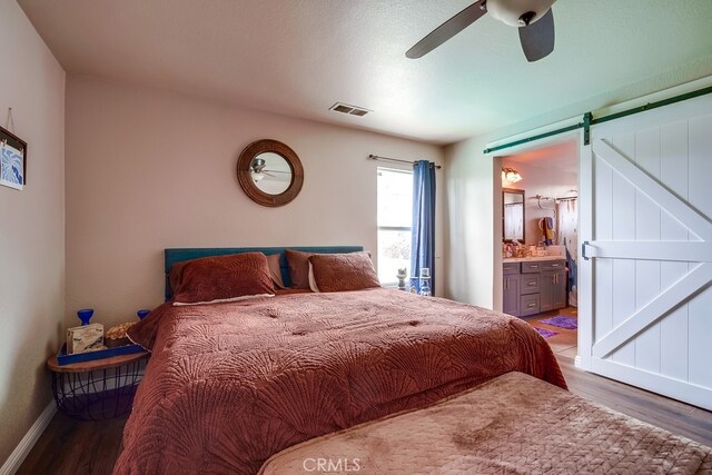 bedroom featuring a ceiling fan, wood finished floors, visible vents, ensuite bath, and a barn door