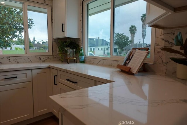 kitchen featuring plenty of natural light, light stone countertops, and white cabinetry