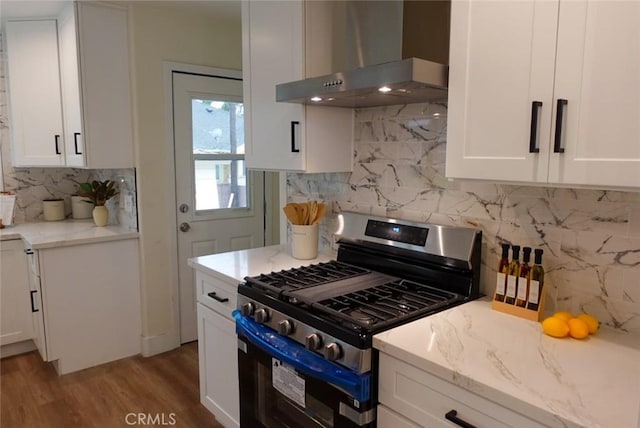 kitchen featuring wood finished floors, white cabinets, wall chimney range hood, gas range, and light stone countertops