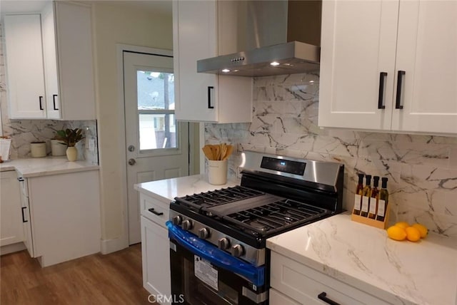 kitchen with white cabinets, wall chimney range hood, light stone countertops, stainless steel gas range, and tasteful backsplash