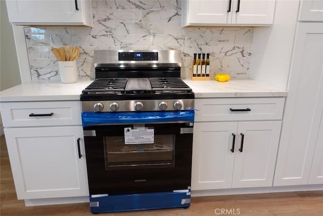 kitchen featuring white cabinets, tasteful backsplash, light stone counters, and stainless steel gas range oven