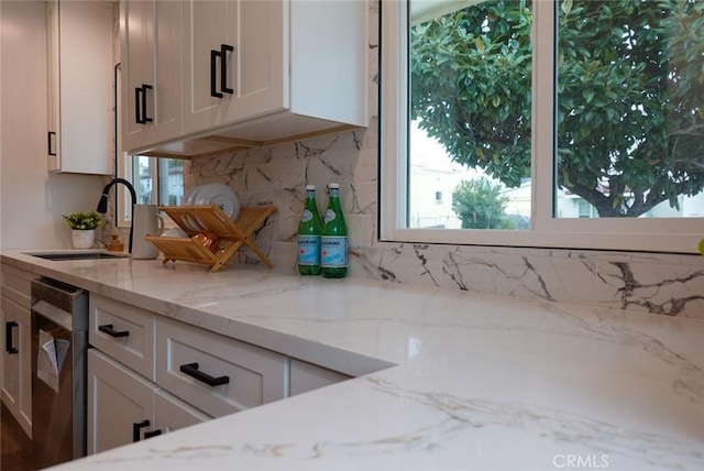 kitchen with light stone counters, decorative backsplash, white cabinets, and a sink