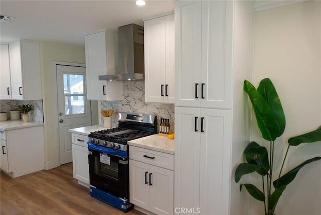 kitchen with white cabinets, tasteful backsplash, gas range, wood finished floors, and wall chimney range hood