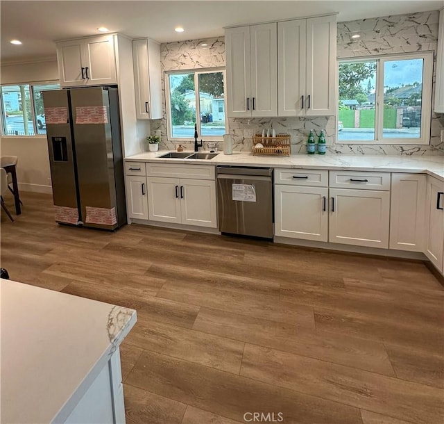 kitchen with light wood finished floors, a sink, tasteful backsplash, appliances with stainless steel finishes, and white cabinetry