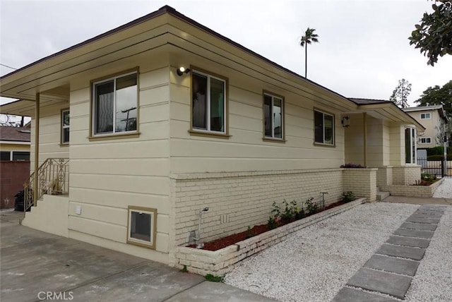 view of side of property featuring a patio area, brick siding, and fence