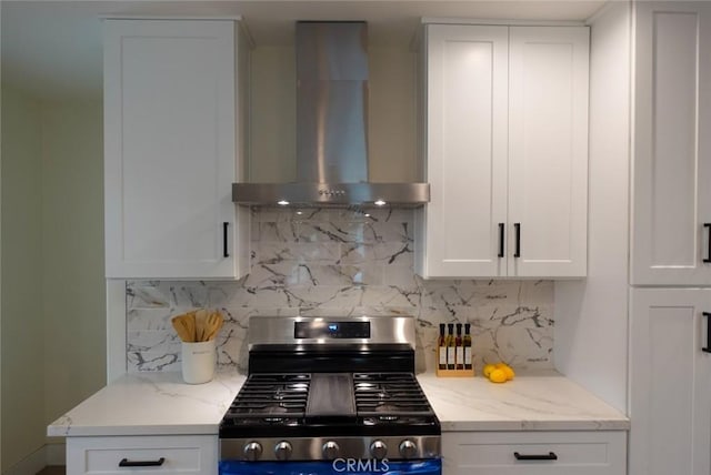 kitchen with stainless steel range with gas stovetop, backsplash, white cabinetry, light stone counters, and wall chimney range hood