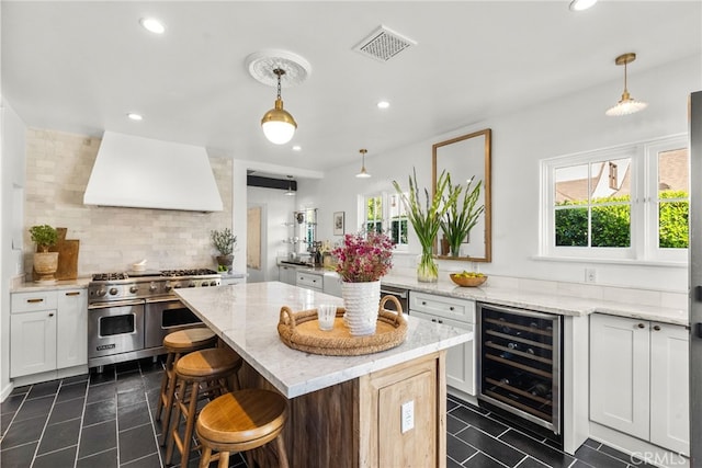 kitchen featuring visible vents, range with two ovens, custom range hood, wine cooler, and a center island