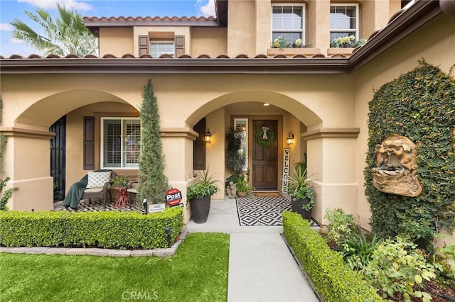 view of exterior entry with a tile roof, covered porch, and stucco siding