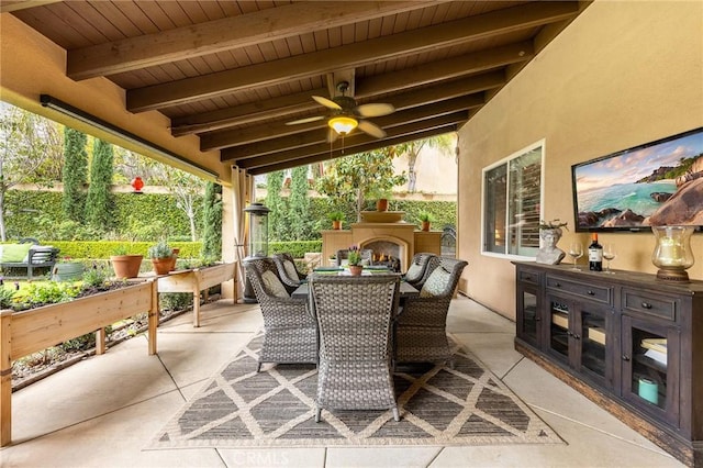 view of patio with outdoor dining area, a ceiling fan, a warm lit fireplace, and an outdoor kitchen