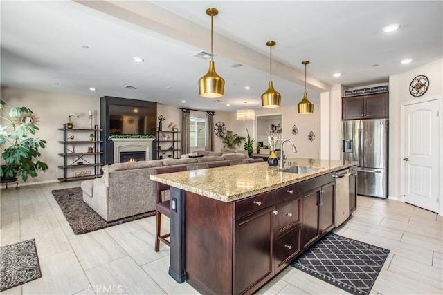 kitchen featuring light stone counters, visible vents, a sink, decorative light fixtures, and appliances with stainless steel finishes