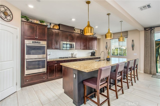 kitchen featuring light stone counters, stainless steel appliances, backsplash, a breakfast bar, and visible vents