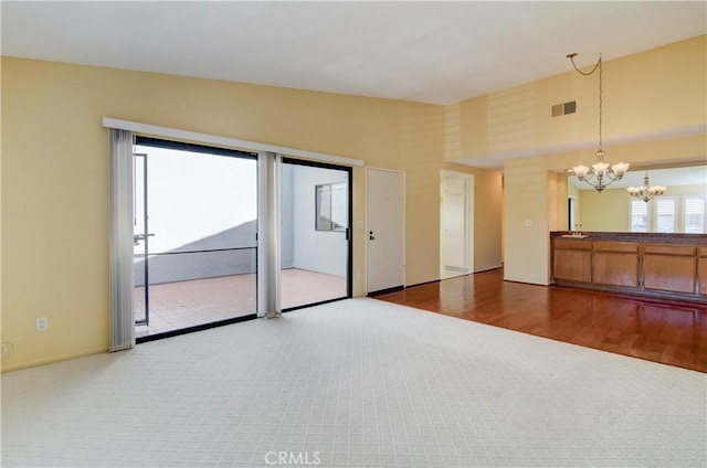 carpeted spare room with a notable chandelier, visible vents, and a towering ceiling