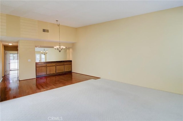 empty room with visible vents, a notable chandelier, and wood finished floors