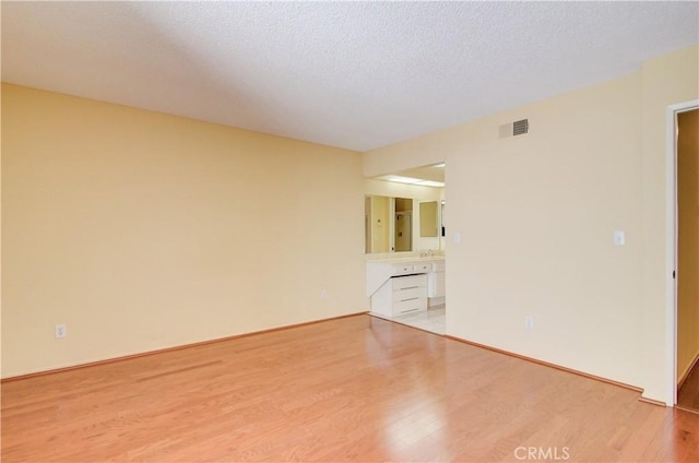 unfurnished room with visible vents, light wood-style flooring, and a textured ceiling