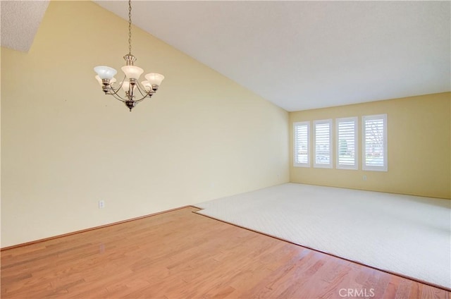 spare room with a chandelier, wood finished floors, and vaulted ceiling