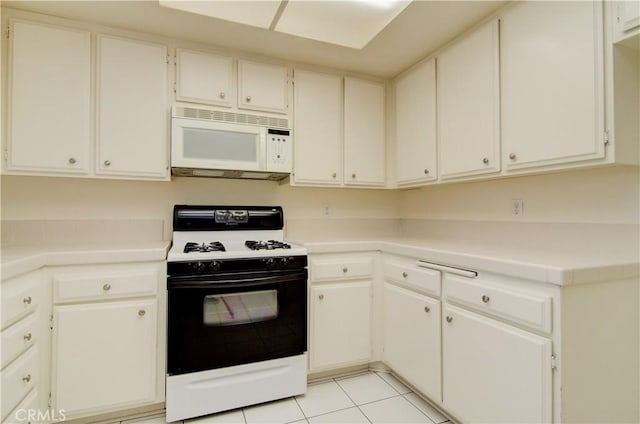 kitchen with white microwave, light tile patterned flooring, light countertops, white cabinetry, and gas range