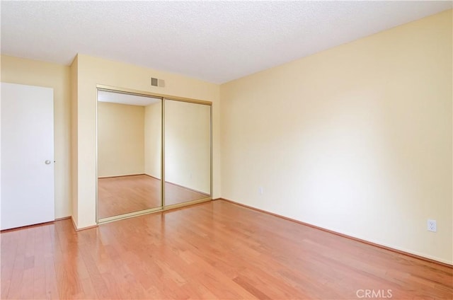 unfurnished bedroom with wood finished floors, visible vents, a closet, and a textured ceiling