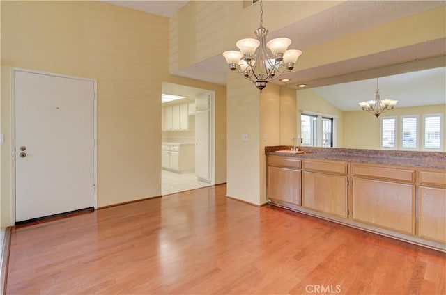 kitchen featuring a sink, an inviting chandelier, light wood finished floors, lofted ceiling, and hanging light fixtures