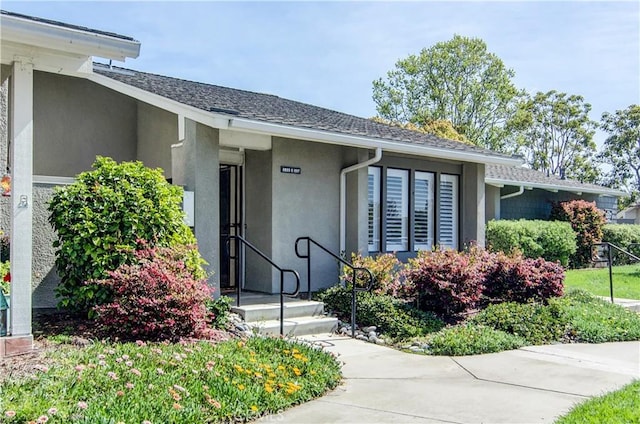 view of exterior entry with roof with shingles and stucco siding