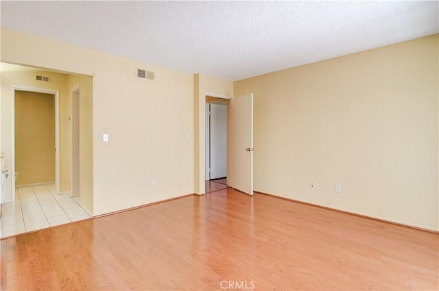 empty room with visible vents, light wood-style flooring, and a textured ceiling