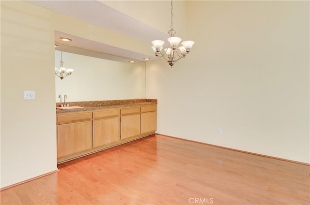 unfurnished dining area with a sink, baseboards, a notable chandelier, and light wood finished floors