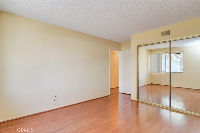 unfurnished bedroom featuring wood finished floors, visible vents, a closet, and a textured ceiling