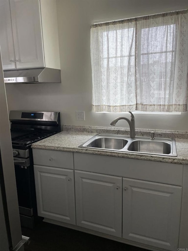 kitchen with gas stove, a sink, light countertops, under cabinet range hood, and white cabinetry