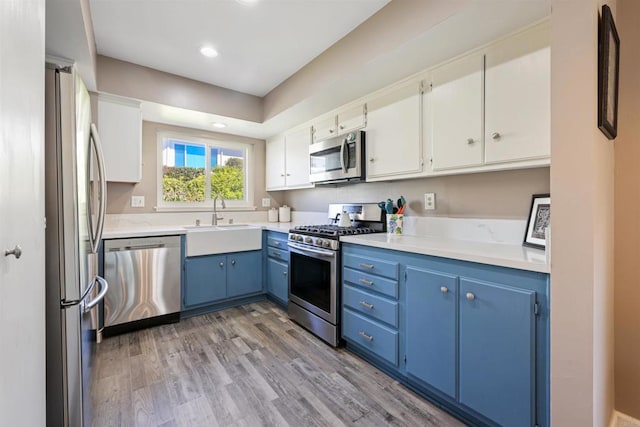 kitchen featuring blue cabinetry, a sink, light countertops, light wood-style floors, and appliances with stainless steel finishes